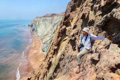 Man with camera on rock formation against sea and sky