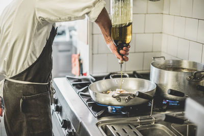 Midsection of chef pouring olive oil from bottle in utensil at kitchen