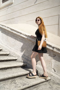 Fashion red hair girl is going up the stairs in a sunny day