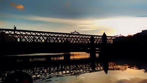 Silhouette bridge over river against sky during sunset