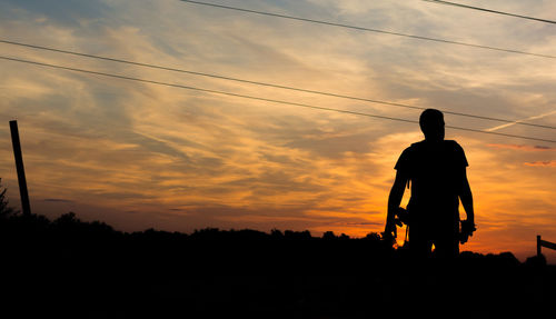 Silhouette man standing on field against sky during sunset