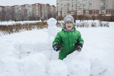 Happy boy standing inside snowcastle and play snowball game in winter park. winter fun in the snow