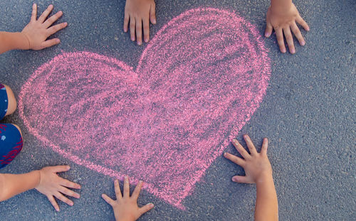 Hands of girls and boy by heart shape drawing on footpath