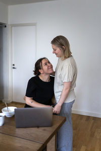 Happy affectionate lesbians embracing by dining table at home