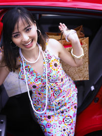 High angle portrait of young beautiful woman holding shopping bags while standing by car