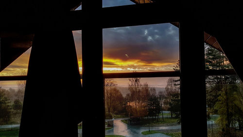 Silhouette trees seen through window during sunset