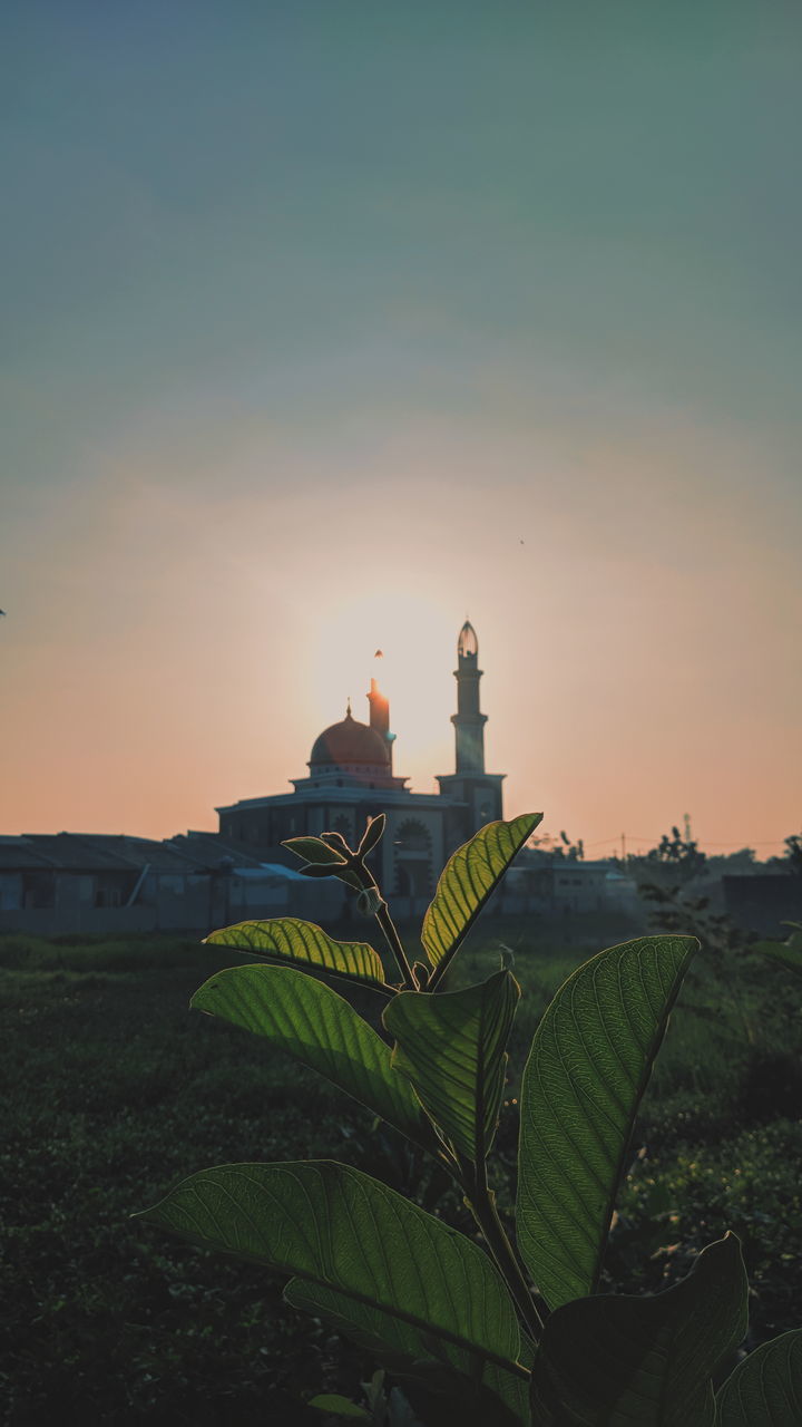 TRADITIONAL BUILDING ON FIELD AGAINST SKY DURING SUNSET