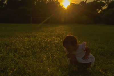Rear view of girl on field against sky during sunset
