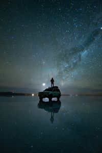 Silhouette man standing on car at beach against star field during night