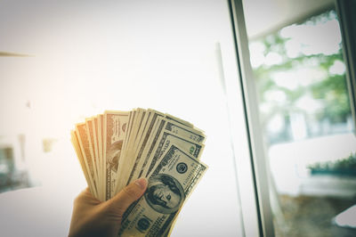 Close-up of hand holding paper against window