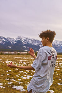 Young man gesturing while standing on field against mountain during winter