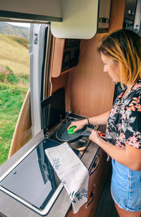 Woman drying pa in camper van while man playing ukulele outdoors