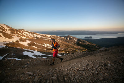 Rear view of man walking on mountain against clear sky