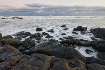 Rocks on beach against sky during sunset