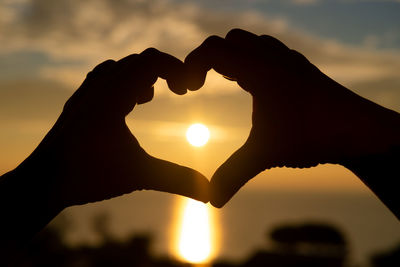 Silhouette hand holding heart shape against sky during sunset