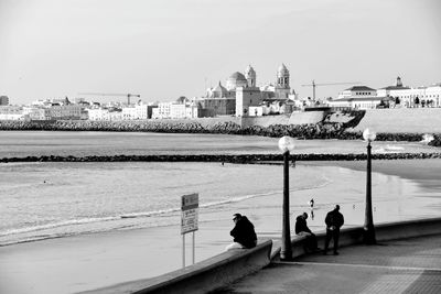 People looking at river in city against clear sky
