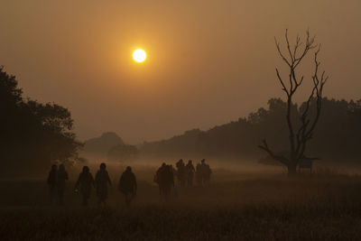 Silhouette people on field against orange sky