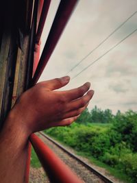 Cropped image of hand on railroad track against sky