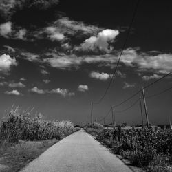 Empty footpath by power lines against sky