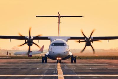 Airplane on runway against sky during sunset