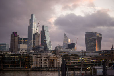 Modern buildings by river against sky in city