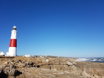 Lighthouse by sea against clear blue sky