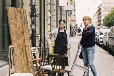 Owner and customer pointing towards chair outside antique shop