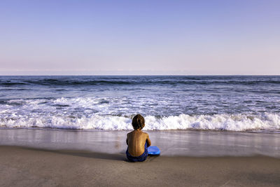 Rear view of 5 years old kid sitting at the beach facing the ocean