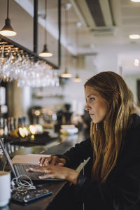 Side view of businesswoman using laptop at bar counter
