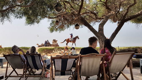 People sitting on table by tree against sky