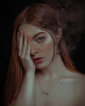 Close-up portrait of young woman covering eye against black background