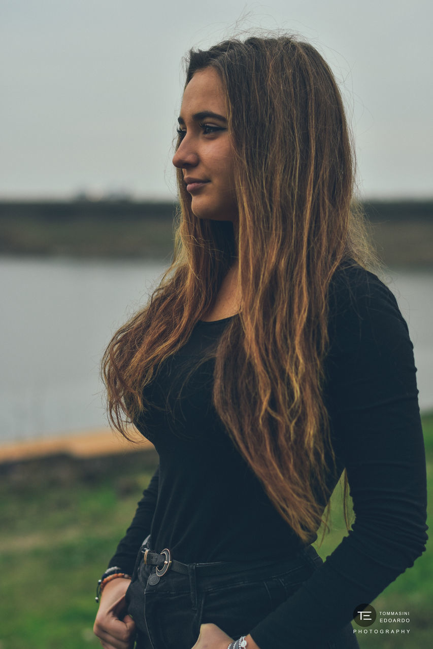 PORTRAIT OF SMILING YOUNG WOMAN LOOKING AWAY OUTDOORS