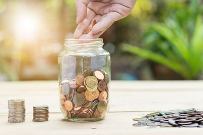 Cropped hand of person pouring coins in jar