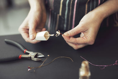 Midsection of woman making wire flower at table