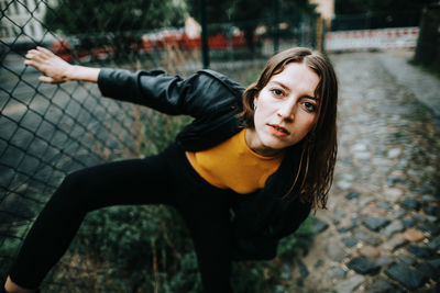 Portrait of young woman standing by fence