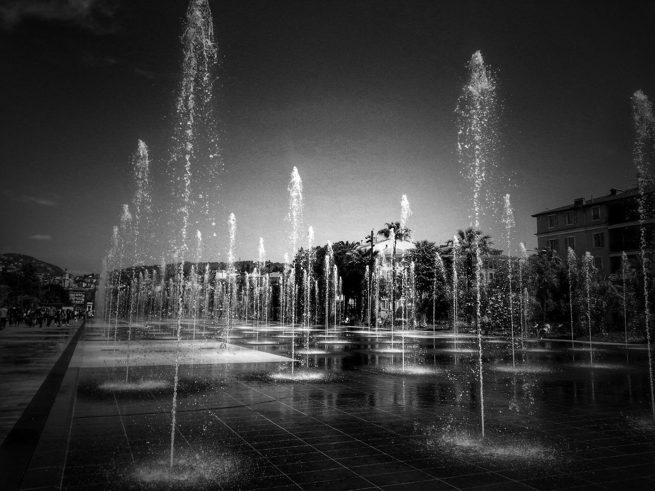 fountain, water, night, spraying, motion, long exposure, illuminated, splashing, tree, reflection, waterfront, sky, blurred motion, wet, outdoors, nature, rain, building exterior, park - man made space, city