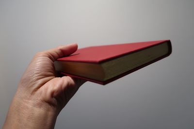 Close-up of hand holding book against gray background