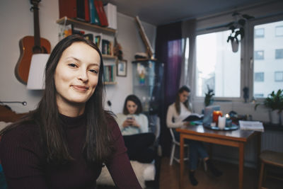 Portrait of happy young woman with female friend sittings in college dorm room