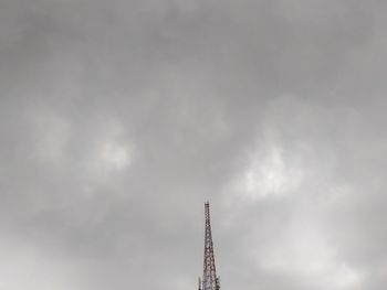 Low angle view of communications tower against cloudy sky