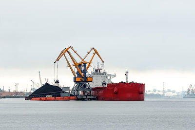 Cranes on pier by sea against sky