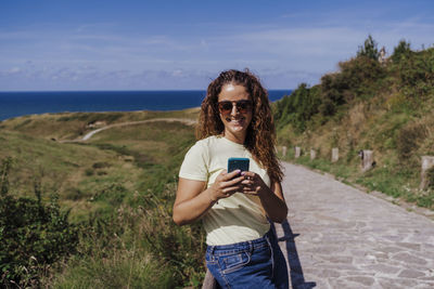 Portrait of smiling young woman using mobile phone against sky