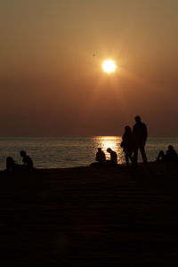 Silhouette people on beach against sky during sunset