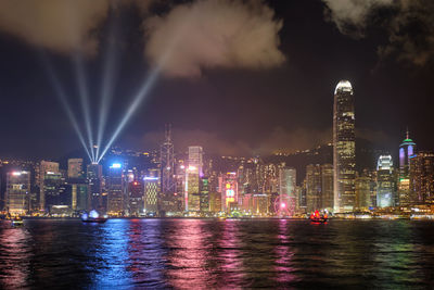 Illuminated buildings by river against sky at night