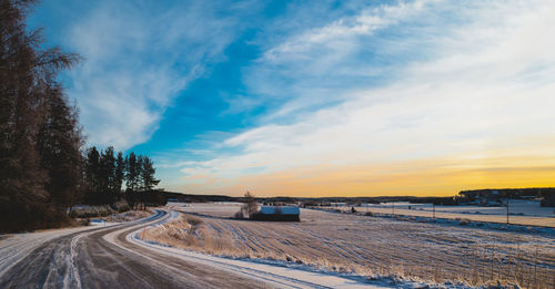 Snow covered landscape against sky during sunset