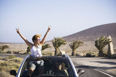 Happy female friends wearing sunglasses standing in convertible against clear sky