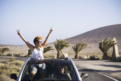 Man sitting on car against road against clear sky