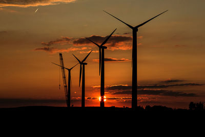 Silhouette of wind turbines and a crane at sunset.