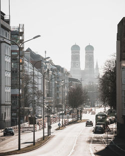 Vehicles on road by buildings against clear sky in city