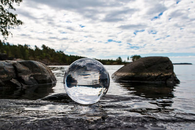 Close-up of crystal ball on rock by river against sky