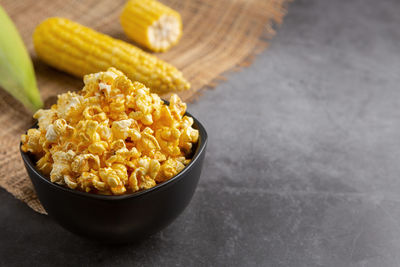 Popcorn in the black bowl and raw corn on the black cement floor.